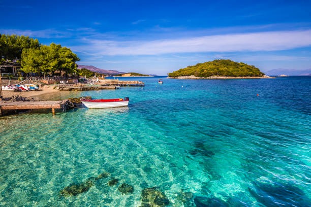 Baía de águas turquesas com barco e ilha verde em Ksamil, na Riviera Albanesa